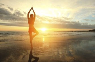 Young woman silhouette practicing yoga on the beach at sunset.